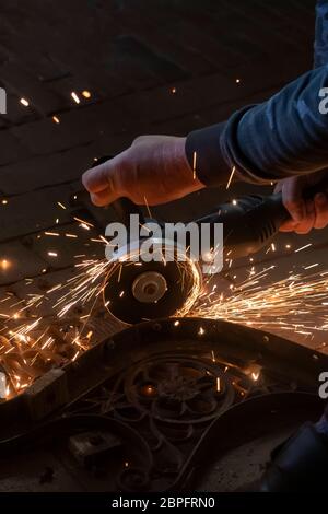 Side view of a man's hands working on a metal part of a garden bench, using an electric grinder while sparks are flying around in the industrial works Stock Photo