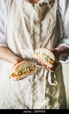 Woman holding fried fish sandwich with tartsre sauce, lemon, arugula Stock Photo