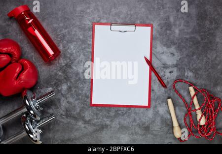 Fitness still life. Sport accessories: dumbbells, rope, boxing gloves and tablet with blank sheet on grey background. Top view. Fitness, sport and hea Stock Photo