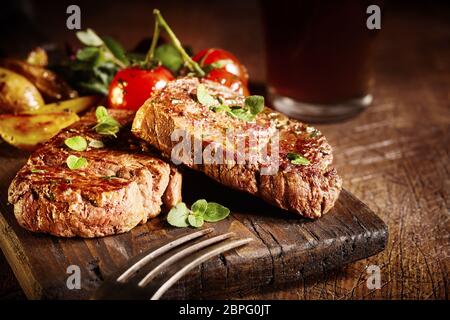 Tender gourmet medallions of roasted or grilled beef fillet seasoned with fresh herbs and spices and served with tomatoes and potato wedges on an old Stock Photo