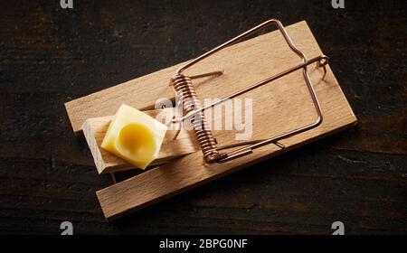 Top view of cocked wooden spring mousetrap loaded with piece of cheese, waiting for rodents on dark wooden surface background Stock Photo