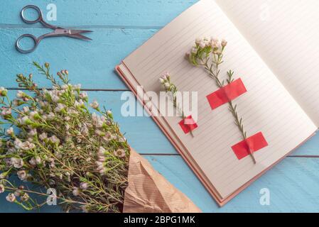 White flowers attached on agenda pages and a flowers bouquet on a blue wooden table, flat lay image Stock Photo