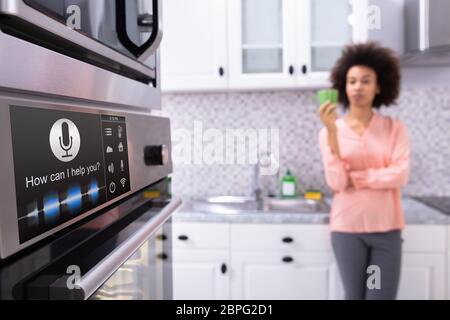 Close-up Of An Oven With Voice Recognition Function Near The Blurred Woman Standing In Kitchen Stock Photo
