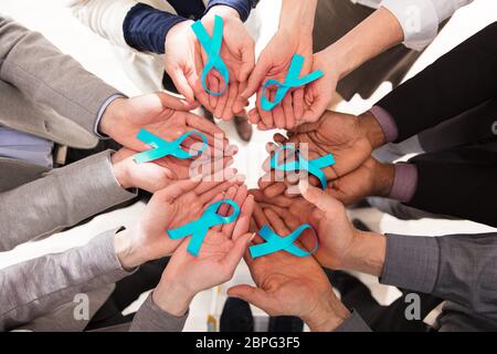 Group Of Businesspeople Holding Teal Ribbons To Support Ovarian Cancer Awareness Stock Photo