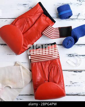 pair of red leather boxing gloves, blue textile bandage, silicone protection for teeth on a white wooden background, top view Stock Photo