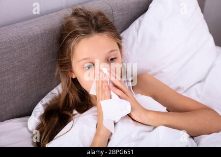 Girl Suffering From Cold Blowing Her Nose With Handkerchief On Bed Stock Photo