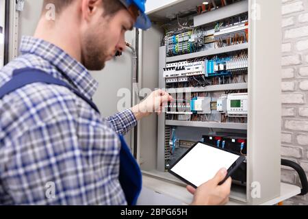 Technician Holding Digital Tablet With Blank Screen In Front Of Fuse Box Stock Photo