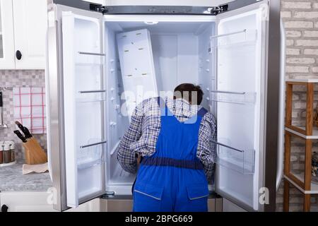 Young Serviceman Checking Fridge With Digital Multimeter Stock Photo