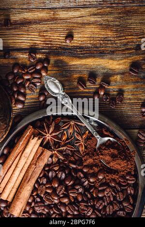 Coffee Beans with Spooonful of Ground Coffee, Cinnamon Sticks and Star Anise on Plate. Some Beans Scattered on Wooden Table. View from Above. Vertical Stock Photo