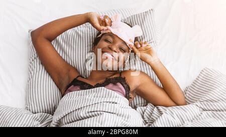 Happy african american girl with braces in bed takes off her sleeping mask