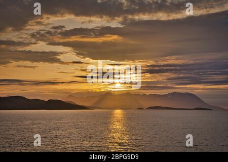 Islands off the west coast of northern Norway seen by the light of the midnight sun with a dramatic sky, clouds and sunbeams shining through Stock Photo