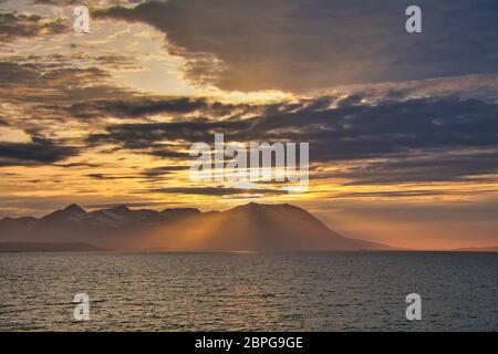 Islands off the west coast of northern Norway seen by the light of the midnight sun with a dramatic sky, clouds and sunbeams shining through Stock Photo