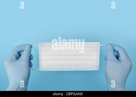 Disposable medical mask in hands in blue rubber medical gloves on a blue background. Healthcare and protection concept. Stock Photo