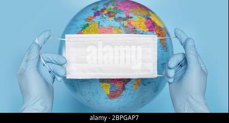 Global coronavirus pandemic. Disposable medical mask in hands on the background of the world globe. Healthcare and protection concept. Stock Photo