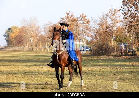 HORTOBAGY, HUNGARY, NOVEMBER, 04. 2018: Hungarian csikos in traditional folk costume showing off his trained horse. Traditional Horse-herdsman of Hung Stock Photo