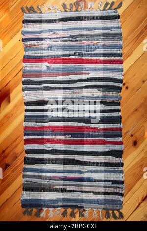 Rustic wicker rug on a wooden floor. Multi-colored Slavic carpet. Stock Photo