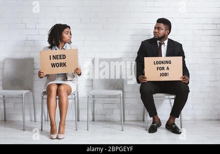 Young vacancy applicants with cardboard job searching signs sitting in company hall, waiting for interview Stock Photo