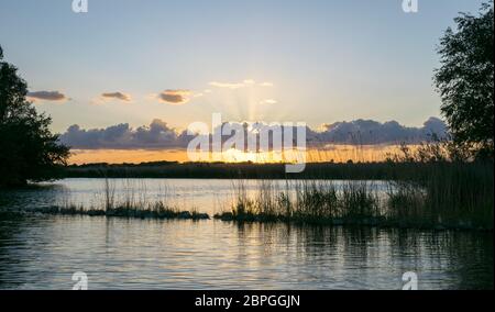 Scenic panorama view of sun beams coming from behind a line of cumulus near a lake in Holland Stock Photo