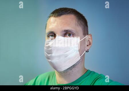 Serious white caucasian man in a disposable protective facial surgical mask as a protection during coronavirus pandemic infection covid-19. Stock Photo