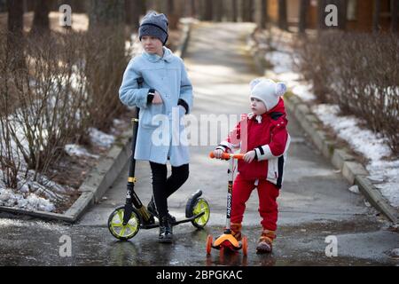 Belarus, the city of Gomel, March 09, 2019. Celebration Maslenitsa.Children with scooters. The older sister and younger brother are playing on the str Stock Photo