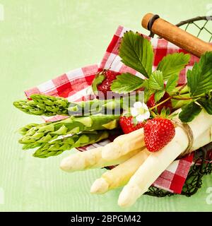Basket with fresh green and white asparagus bunches decorated with ripe strawberry. Viewed from above in close-up Stock Photo