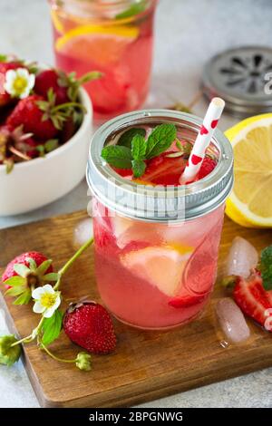 Summer drink refreshing. Lemonade with fresh strawberries, ice and lemons on a light stone countertop. Stock Photo