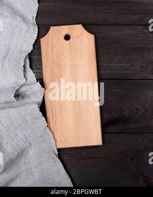 rectangular empty wooden cutting board on a gray linen napkin, brown table Stock Photo