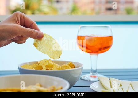 closeup of a young caucasian man taking a potato chip from a bowl placed on a table next to different other snacks and a glass with a red drink Stock Photo