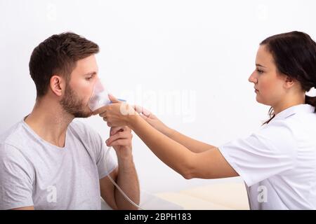 Side View Of Young Female Doctor Holding Oxygen Mask Over Male Patient's Mouth Stock Photo