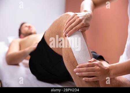 Close-up Of A Therapist Waxing Female Customer's Leg At Beauty Spa