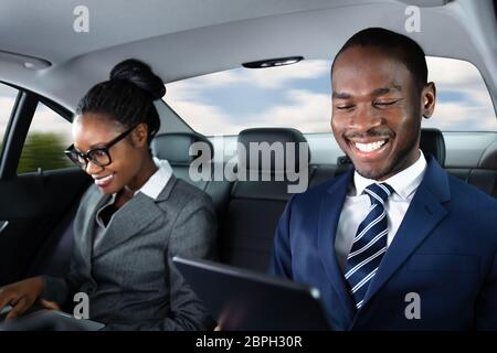Two Happy African Businesspeople Using Electronic Devices While Traveling By Car Stock Photo