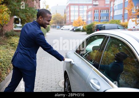 Side View Of Smiling Young African Male Valet Opening Car Door Stock Photo
