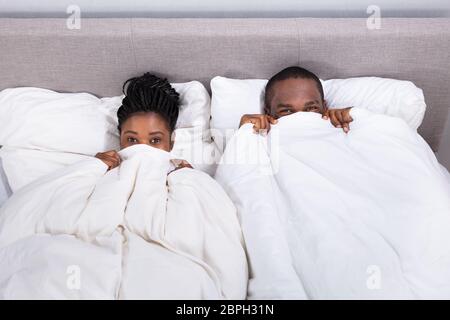 High Angle View Of An African Couple Trying To Hide In Blanket Stock Photo