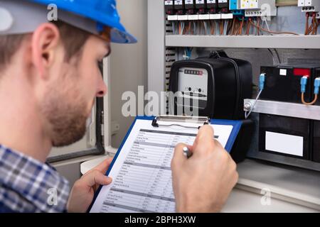 Close-up Of Male Technician Writing On Clipboard In Front Of Fuse Box Stock Photo