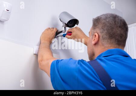 Close-up Of Male Technician Adjusting Cctv Camera On Wall With Screwdriver Stock Photo