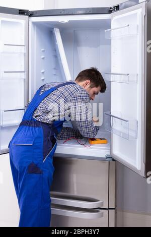 Young Serviceman Checking Fridge With Digital Multimeter Stock Photo