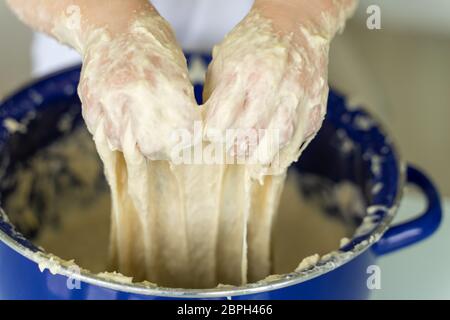 little girl kneads yeast dough in a blue pan, hands closeup. Stock Photo