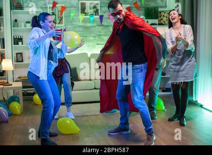 Beautiful young woman holding a balloon at a party and looking at her friend dressed up like a super hero. Stock Photo