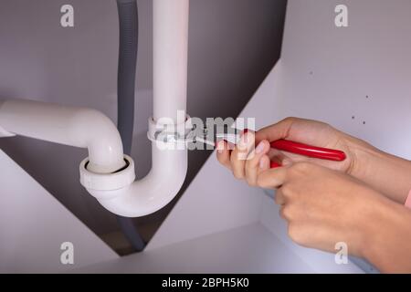 Close-up Of A Concentrated Young Woman Repairing White Sink Pipe With Adjustable Wrench Stock Photo