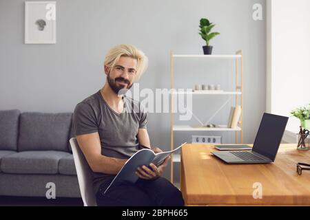 Online learning. Happy guy is preparing a project for a lesson using a laptop video call course sitting at a table at home. Stock Photo