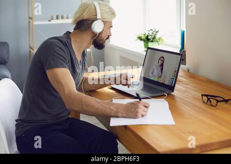 University college online education. A guy student in headphones teaches a lecture online with a teacher video call with a laptop while sitting at Stock Photo