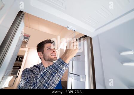 Young Male Technician Checking Refrigerator With Screwdriver Stock Photo