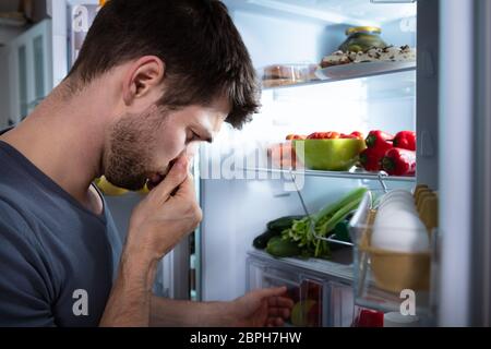 Side View Of Young Man Recognizing Bad Smell Coming From The Refrigerator Stock Photo