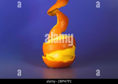 Orange with peeled spiral skin on violet-blue background. Stock Photo