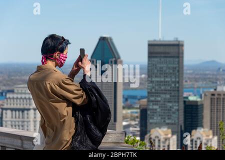 Montreal, CA - 18 May 2020 : Young woman wearing face mask amid coronavirus outbreak taking a picture from Montreal Skylne. Stock Photo