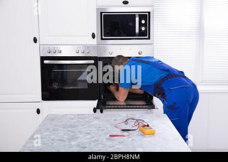 Mature Technician In Overall Repairing Oven In Kitchen Stock Photo