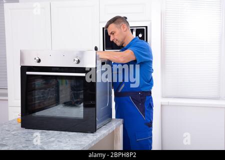Mature Male Technician Repairing Oven On Kitchen Worktop Stock Photo