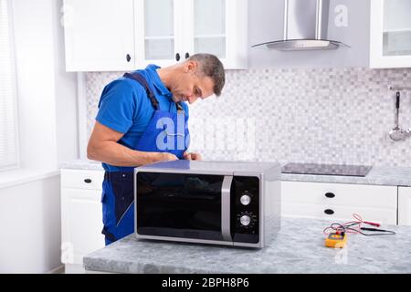Side View Of Mature Man Repairing Microwave Oven In Kitchen Stock Photo