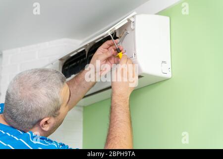 Male technician - repair and diagnostics of air conditioners. Opening the cover and removing the display for repair Stock Photo
