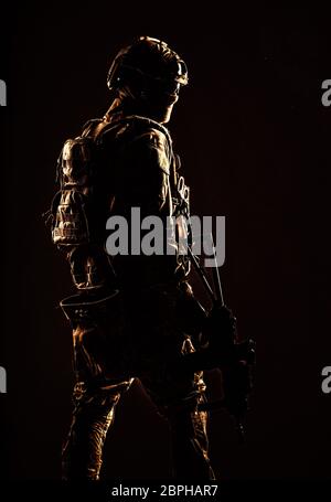Low key studio shoot of army special forces soldier, commando fighter in mask, ballistic glasses, tactical helmet and battle uniform, holding short ba Stock Photo